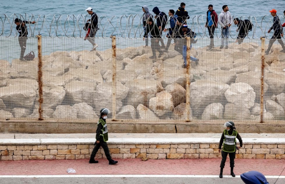 Agentes de seguridad marroquíes montan guardia mientras un grupo de migrantes caminan por la costa en la ciudad norteña de Fnideq, en un intento de cruzar la frontera de Marruecos al enclave español de Ceuta, este martes.