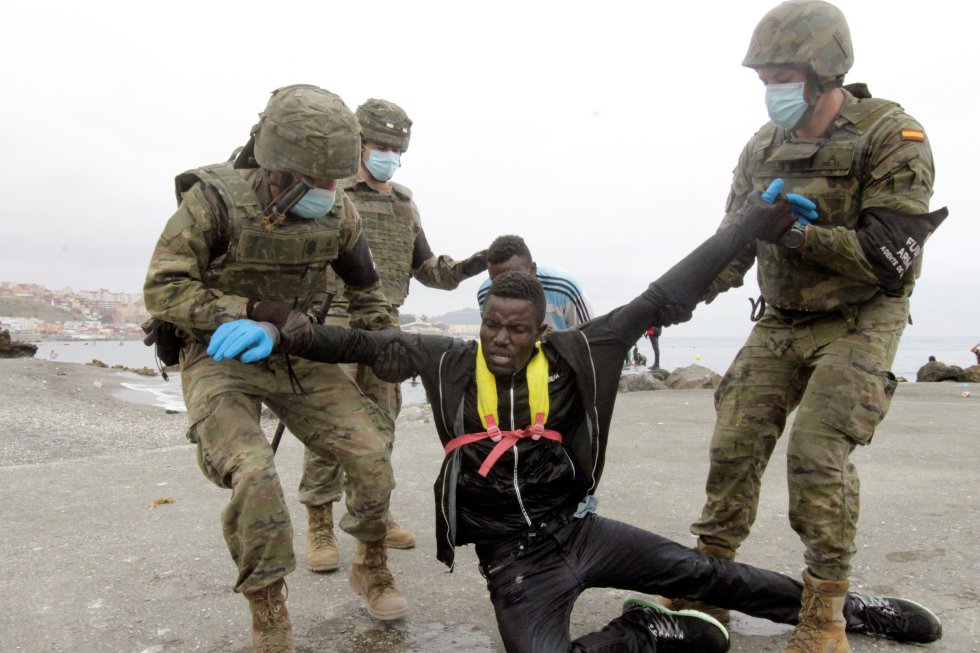 Miembros del Ejército de Tierra ayudan a dos inmigrantes que han logrado cruzar uno de los espigones fronterizos de Ceuta.